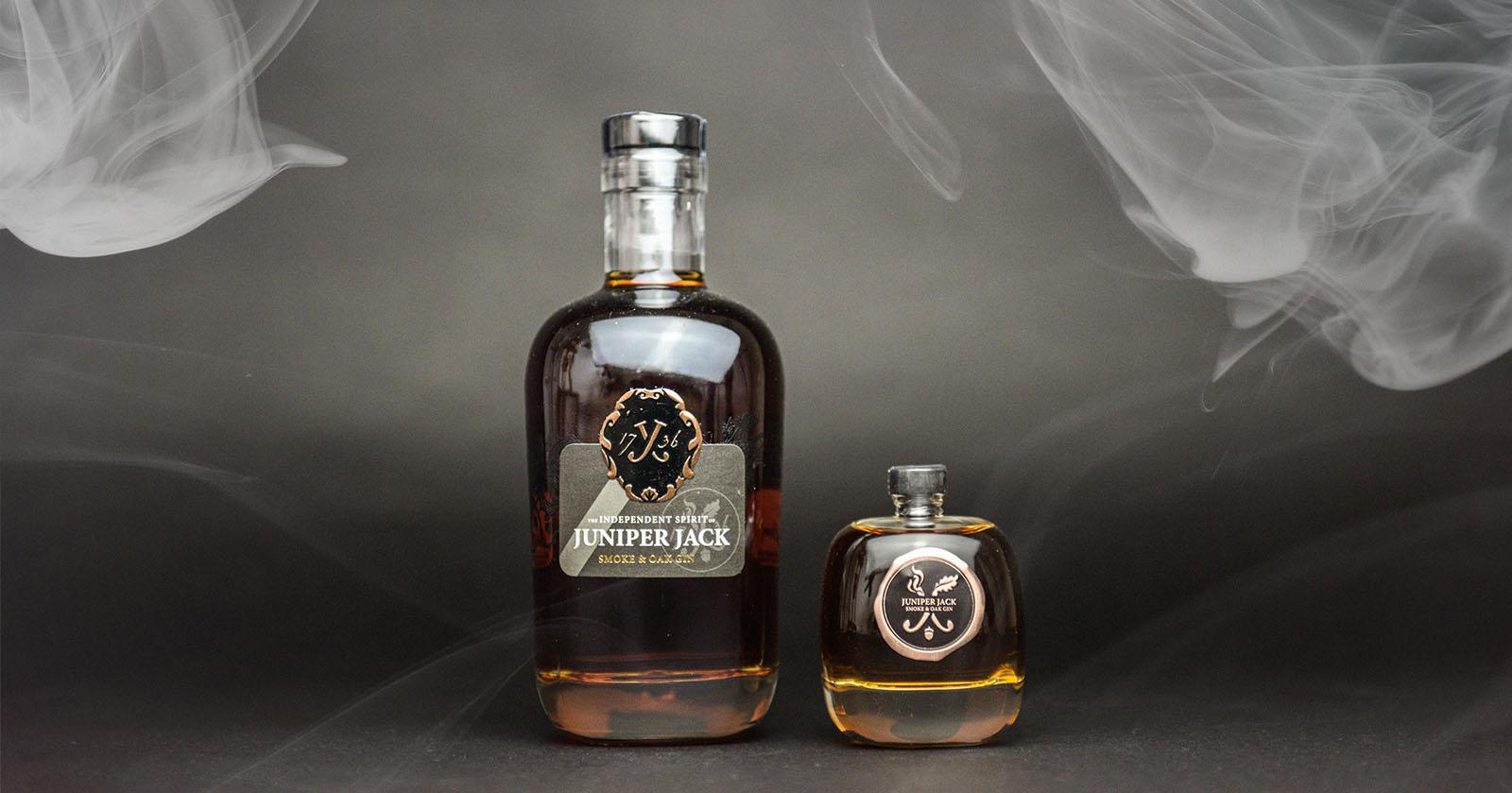 Entdecke den einzigartigen Geschmack des Juniper Jack Smoke & Oak - intensiver Wacholder trifft auf süße Rauchigkeit und Karamellnoten aus der Eichenfasslagerung." (Bild zeigt eine Flasche des Gins mit rauchigen Holzfässern im Hintergrund)