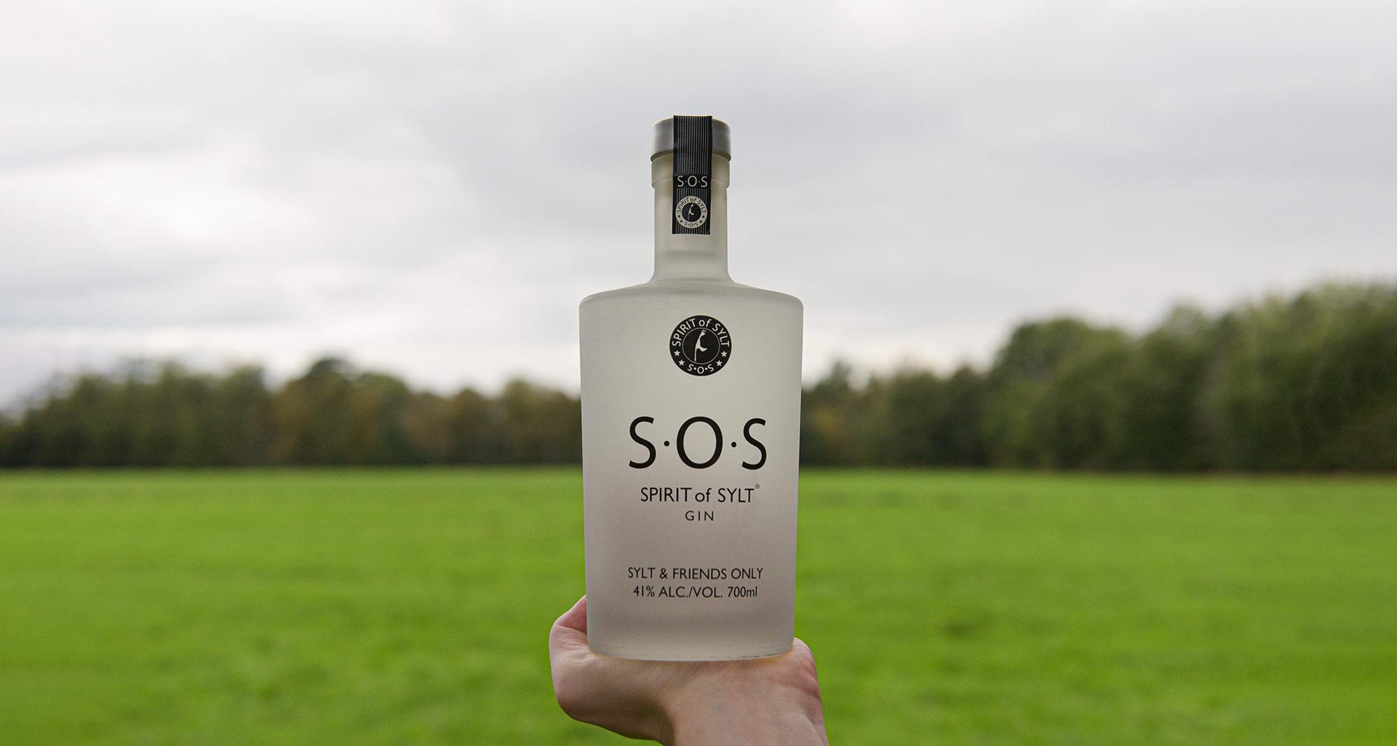 Eine Flasche des S.O.S. Spirit of Sylt Premium Gin auf einem schlichten, weißen Hintergrund mit einem Etikett in blauen Farben, das einen Sylter Leuchtturm zeigt und den Namen des Gins trägt.